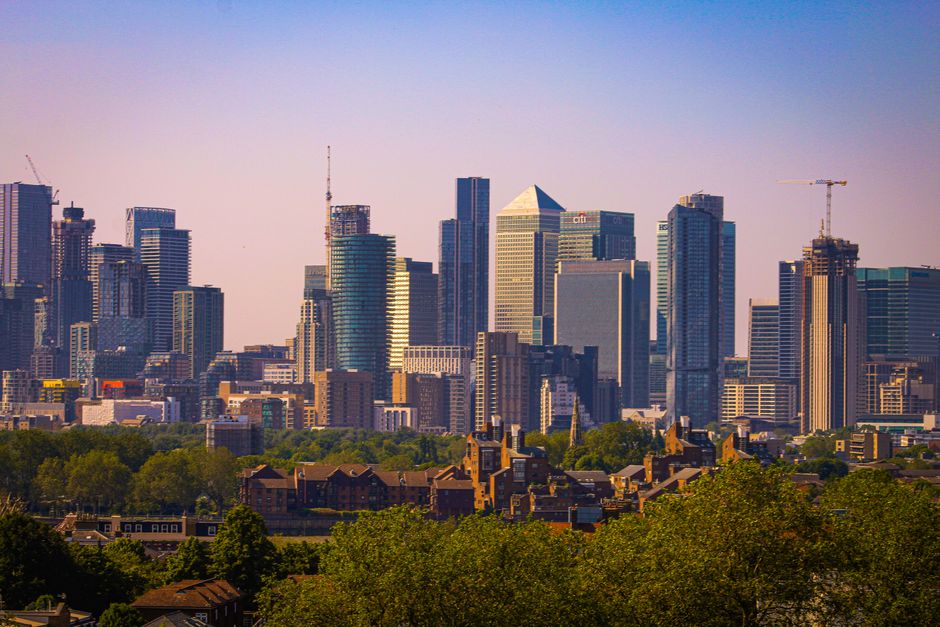 A panoramic view of a modern city skyline featuring a variety of high-rise office buildings and residential towers constructed with glass facades that reflect sunlight, creating a shimmering effect. T